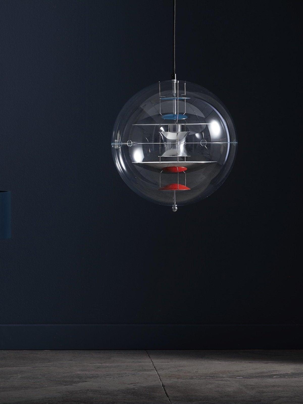 Chrome-tone reflector globe on a black cord against a dark-blue wall, with small blue and red discs inside