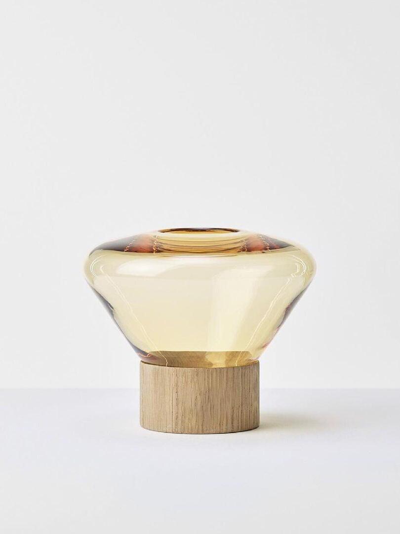 Isolated pale amber-yellow rounded glass shade with top opening on light wood base