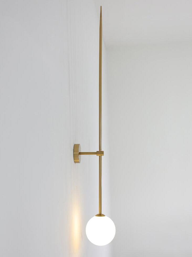 Side view of a lit gold-tone rod wall light with a round backplate and glowing white globe