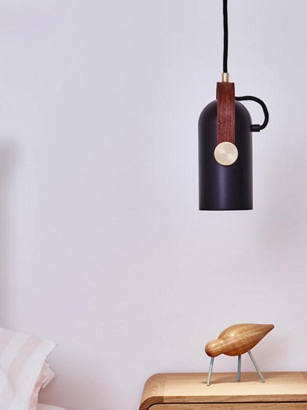 Vertical black pendant above a wooden bedside cabinet and bird ornament, with white bedding at left