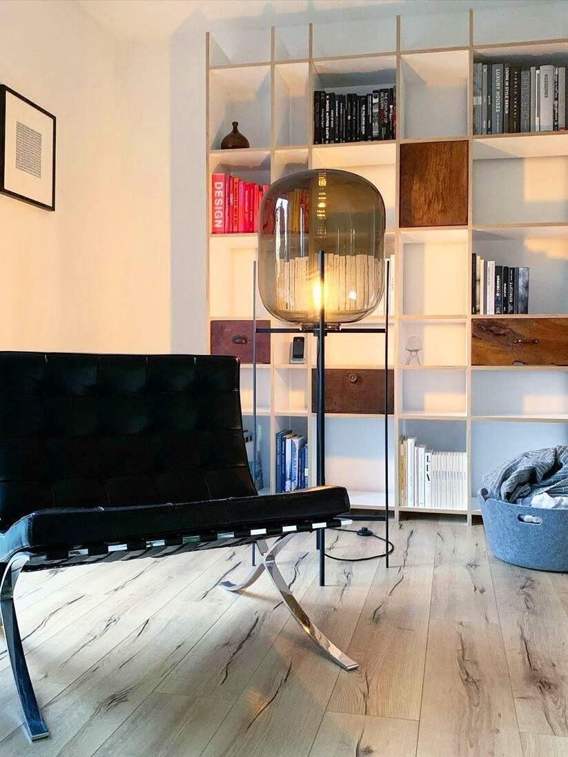 Amber Oda lamp on a black stand beside a bench and open shelving.