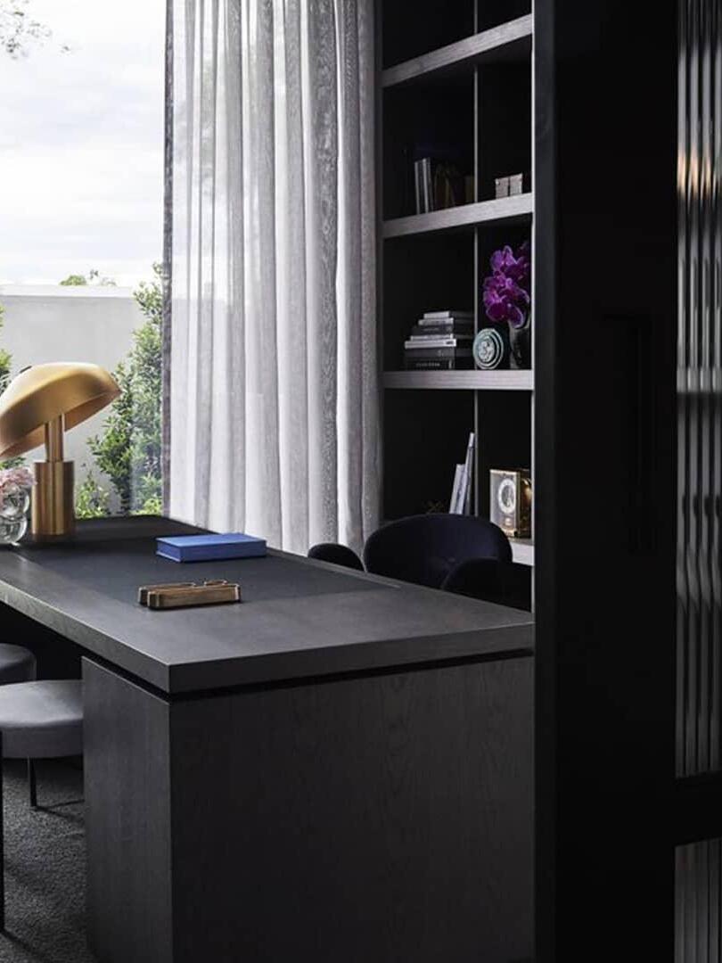 Gold table lamp by tall window and dark desk