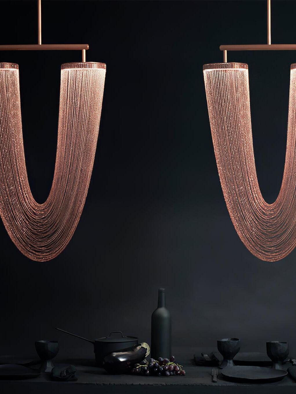 Two rose-gold chain pendants against a dark wall