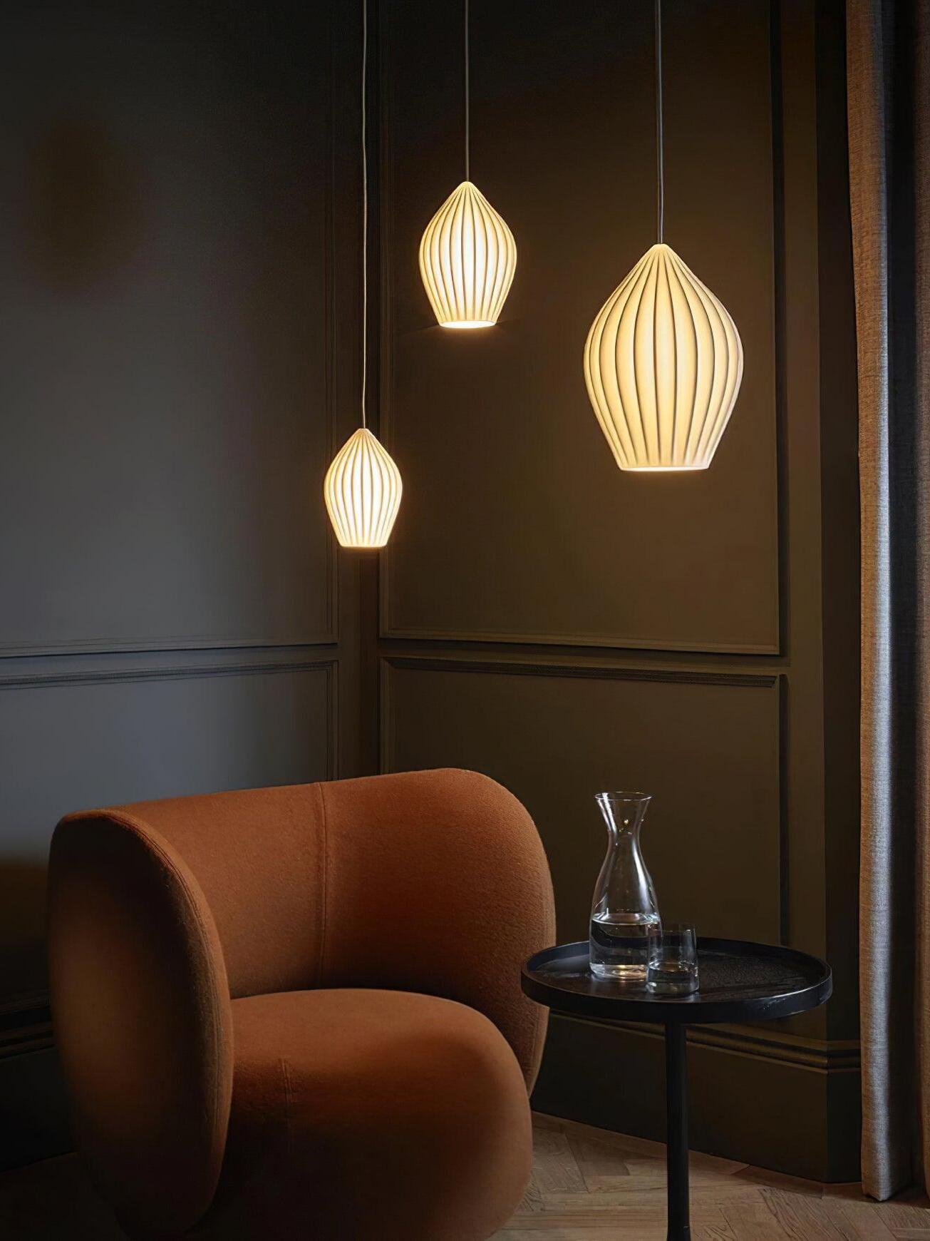 Three glowing ribbed pendant shapes at different heights above an armchair and side table
