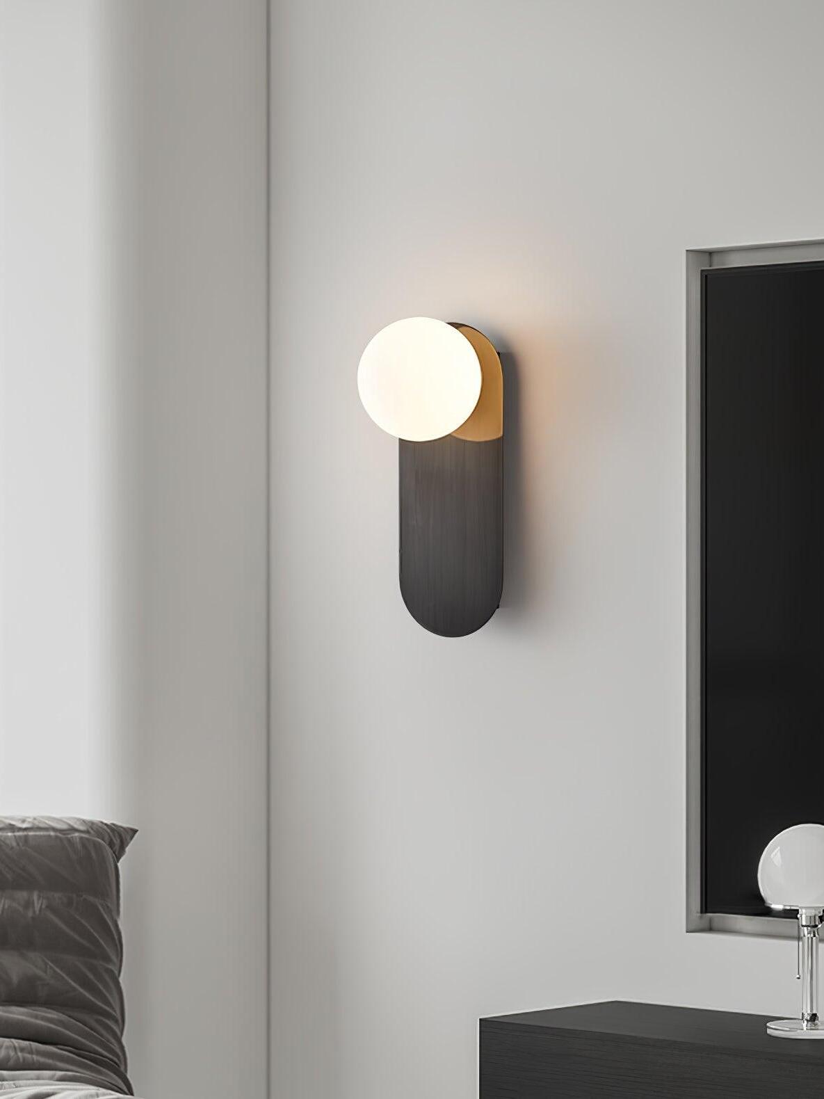Black globe sconce with a long rounded plate against a pale wall