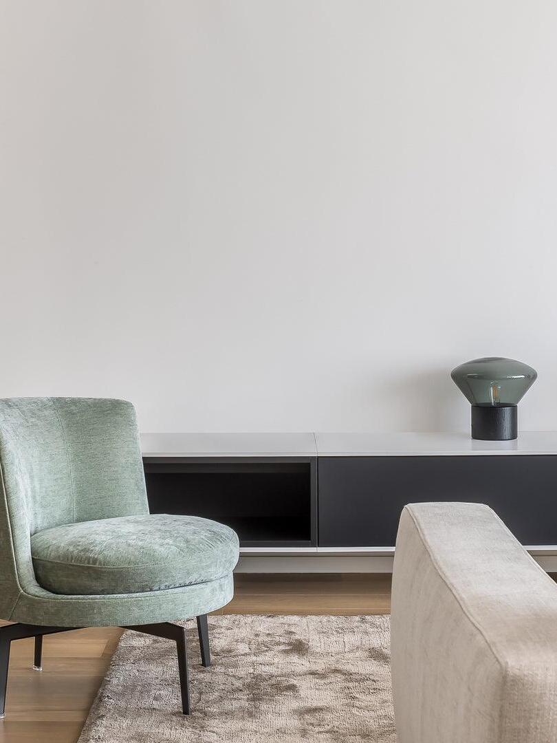Small green-smoke glass lamp on dark cabinet near upholstered chairs
