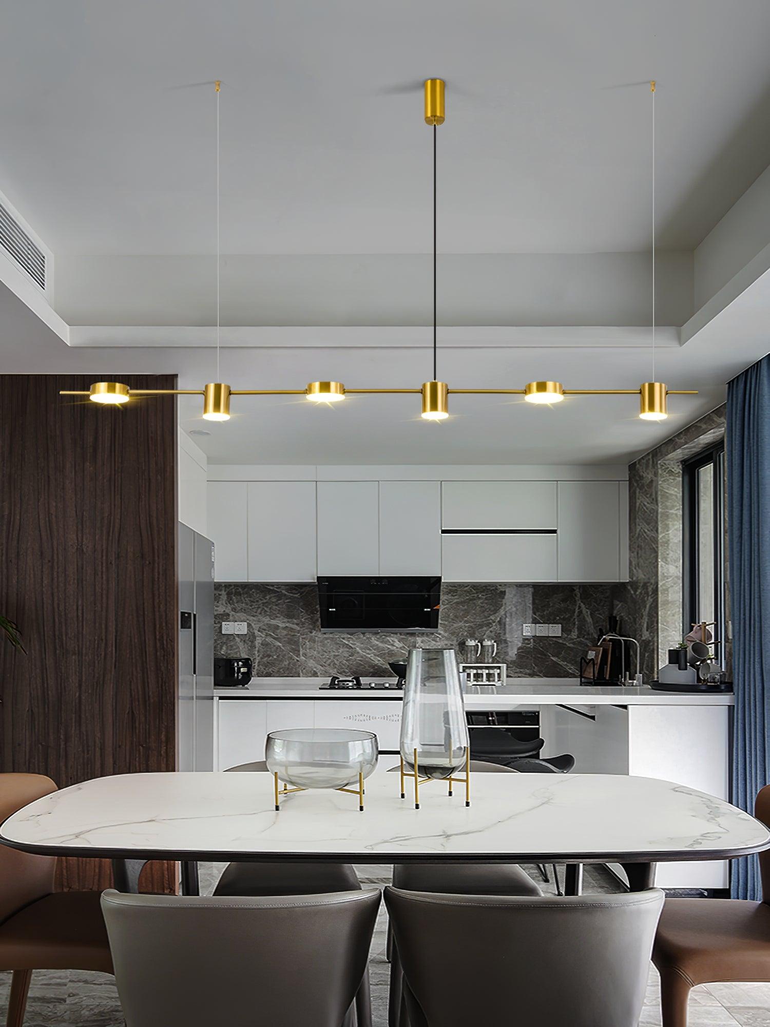Gold linear pendant above a pale dining table in an open kitchen