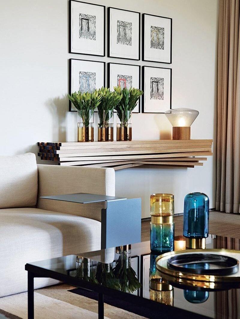 Small glass and wood lamp on console beside flower vases and wall art