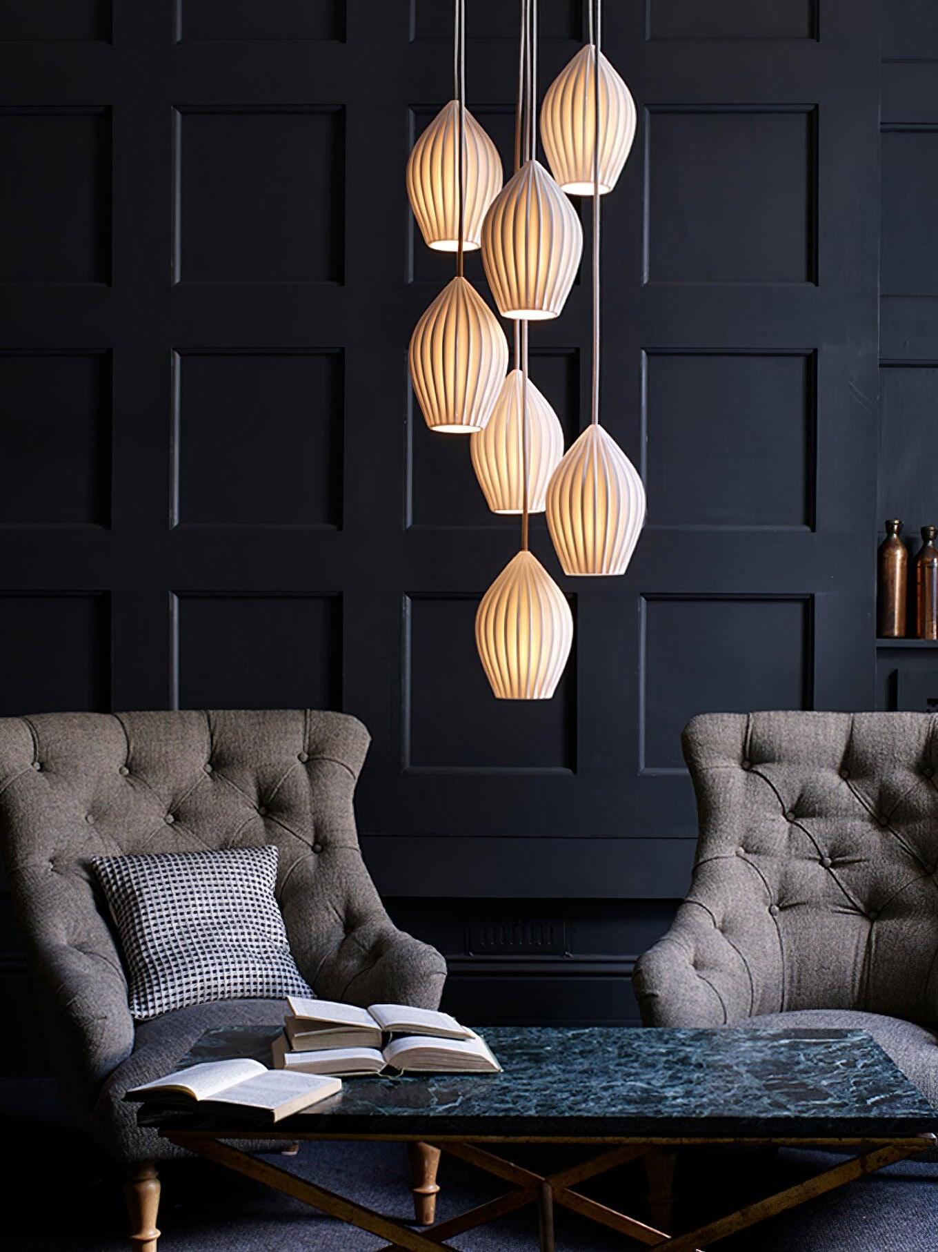 Multi-pendant arrangement of glowing ribbed shades above seating against a dark panelled wall
