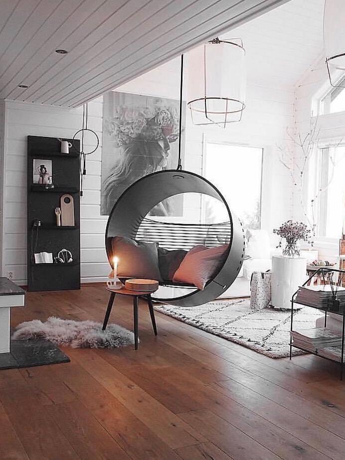 White fabric lantern pendant above a circular hanging chair, with wooden floor, white shelves and side table