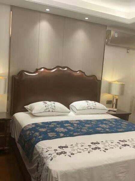 Bedroom with dark upholstered headboard, bedside lamps and patterned bedcover