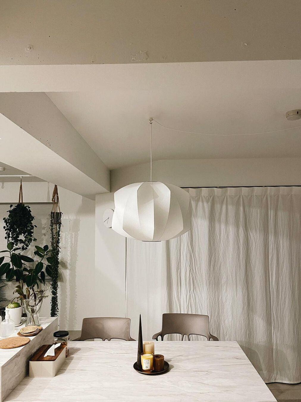 White twisting-panel pendant above a pale dining table with a cord routed to a ceiling hook