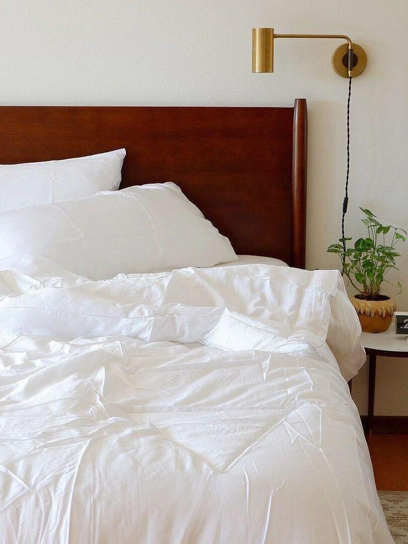 Brass-tone light above bedside table by reddish wood headboard