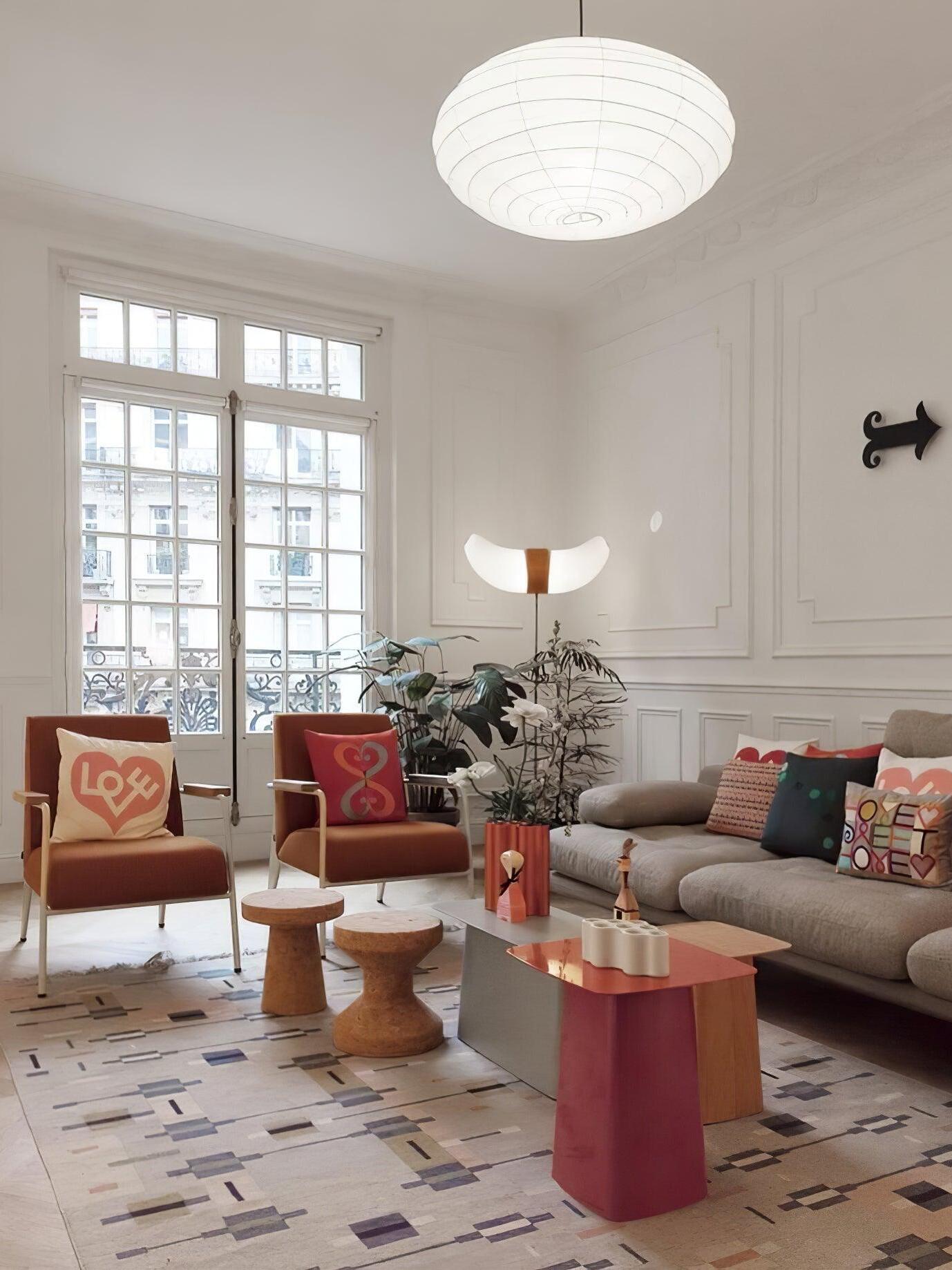 Illuminated paper lantern above a colourful living room with red chairs, grey sofa, tall windows and abstract tables