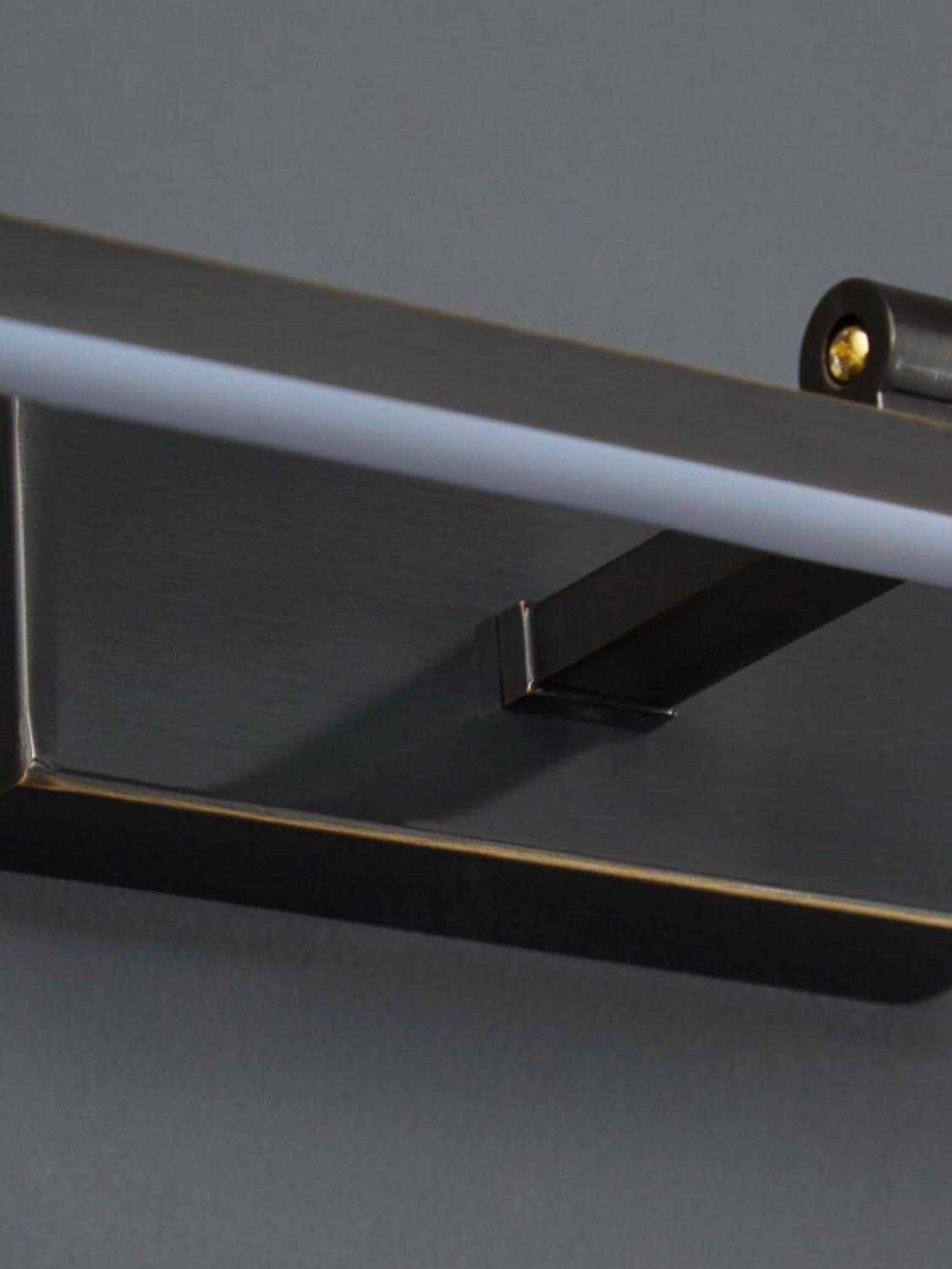Close-up of pale underside strip on black light bar, projecting support arm and rectangular wallplate with gold-tone edges