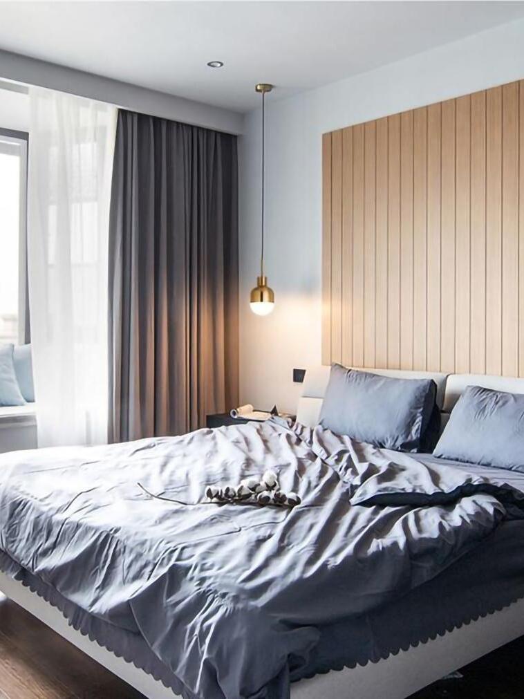 Single lit Niku pendant beside a gray bed with a wood-panel headboard and curtains