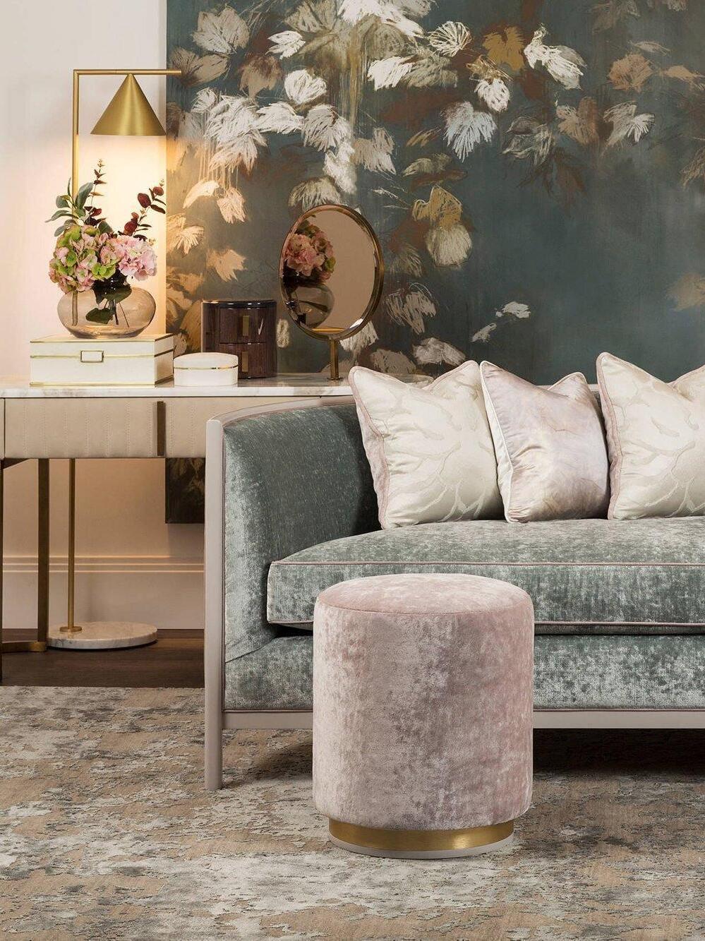 Gold-tone lamp on console near green sofa and floral wallpaper