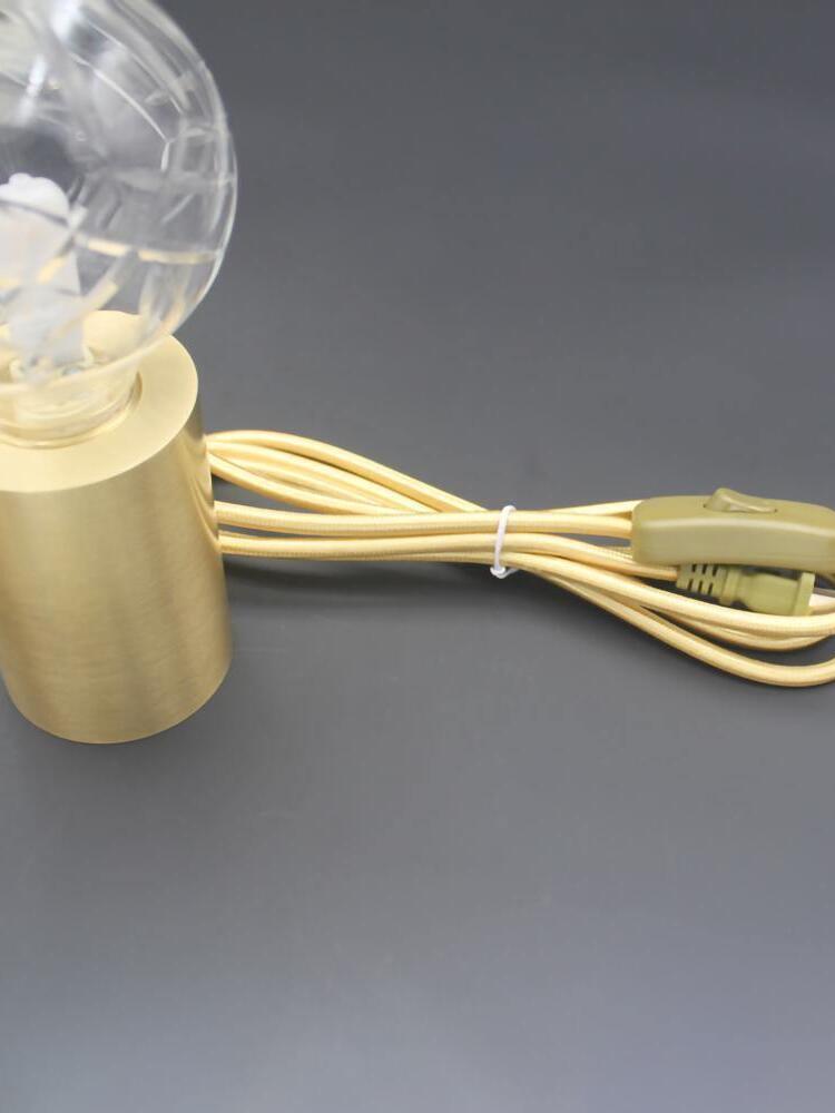 Inline switch on gold-colour cord beside cylindrical lamp base
