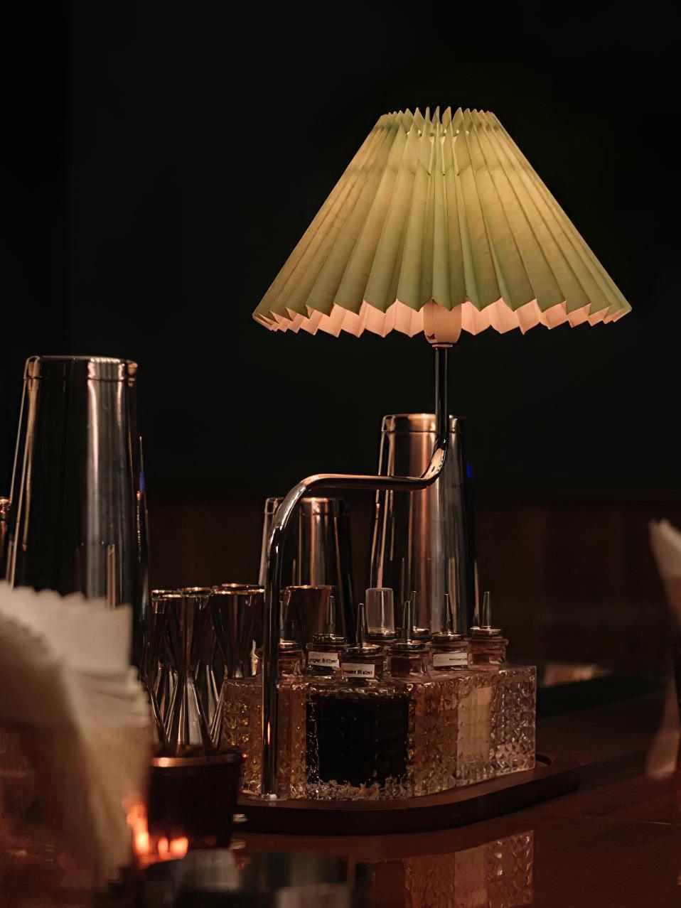 Pleated table lamp glowing among glasses in dark room