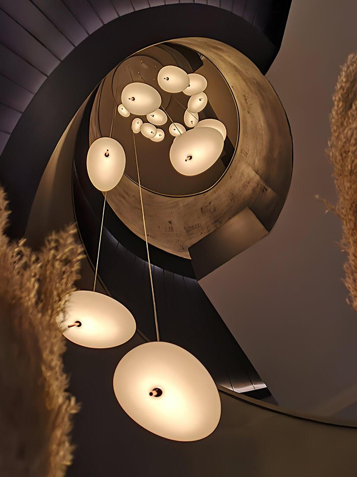 Upward view of numerous glowing white pendant shades suspended through a spiral stairwell