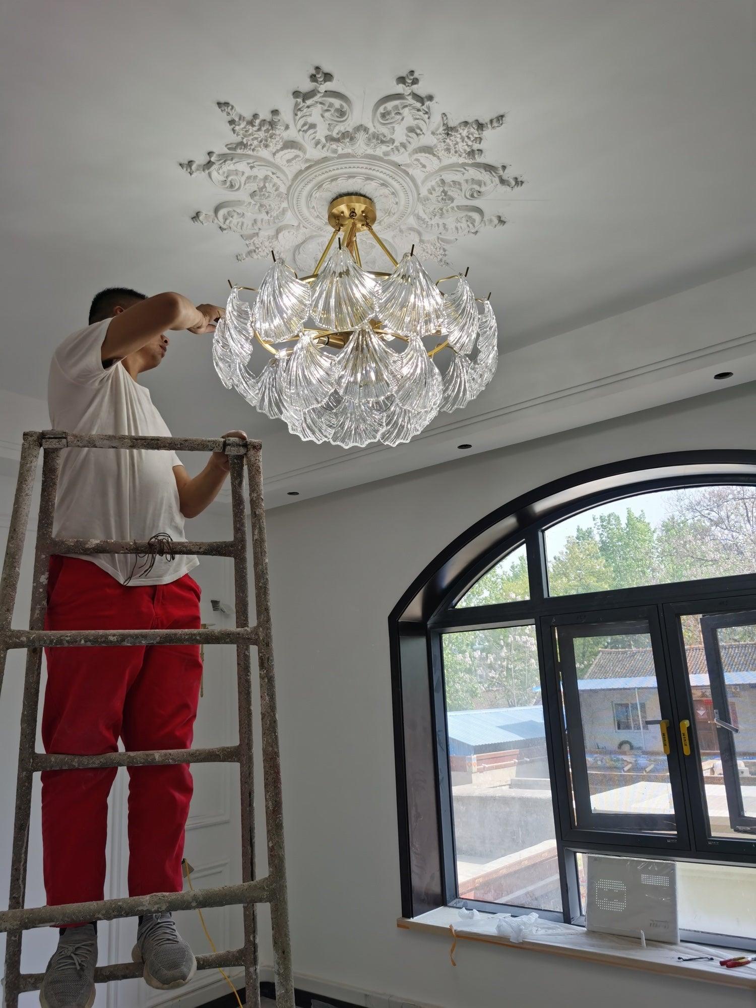 Person on a ladder beside the shell-panel ceiling light near ceiling decoration and a window