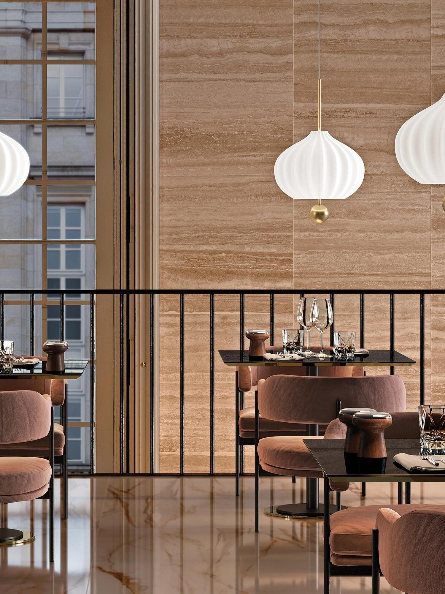 White fluted pendant with brass ball above restaurant tables and pink chairs beside a wood-framed window