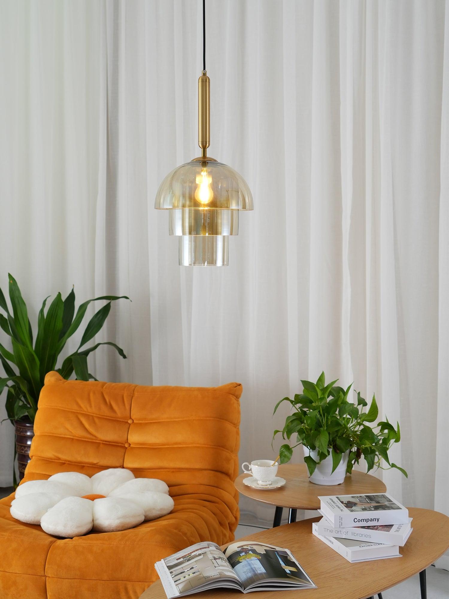 Lit three-tier glass pendant above an orange chair with flower cushion, plants, wood tables, books and white curtains