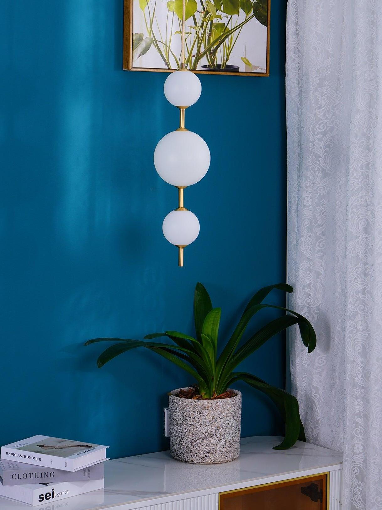 Three white globes with brass-tone links above a cabinet and plant against a teal wall