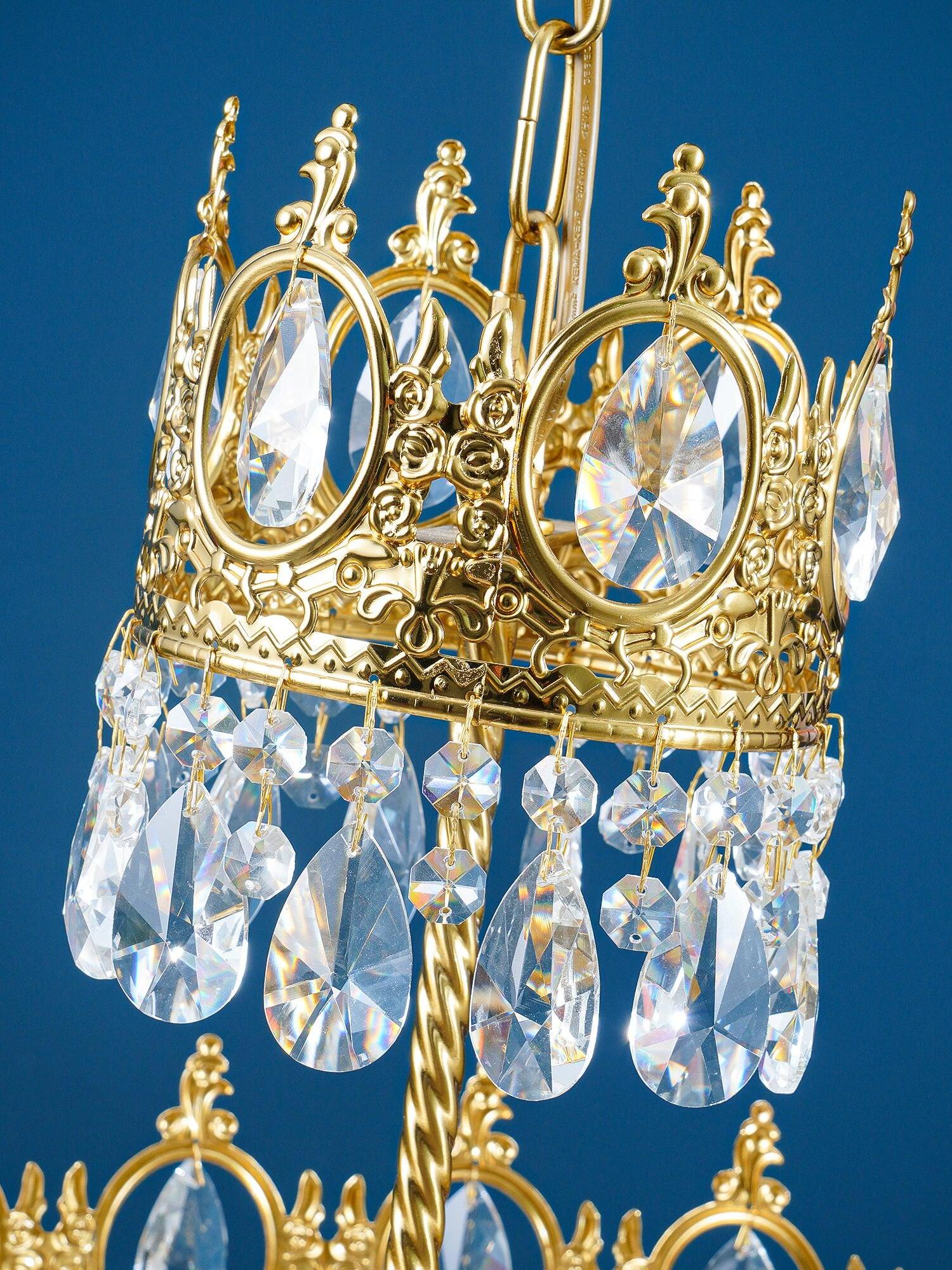 Close upper crown ring with oval faceted crystals and dangling drops against a blue background