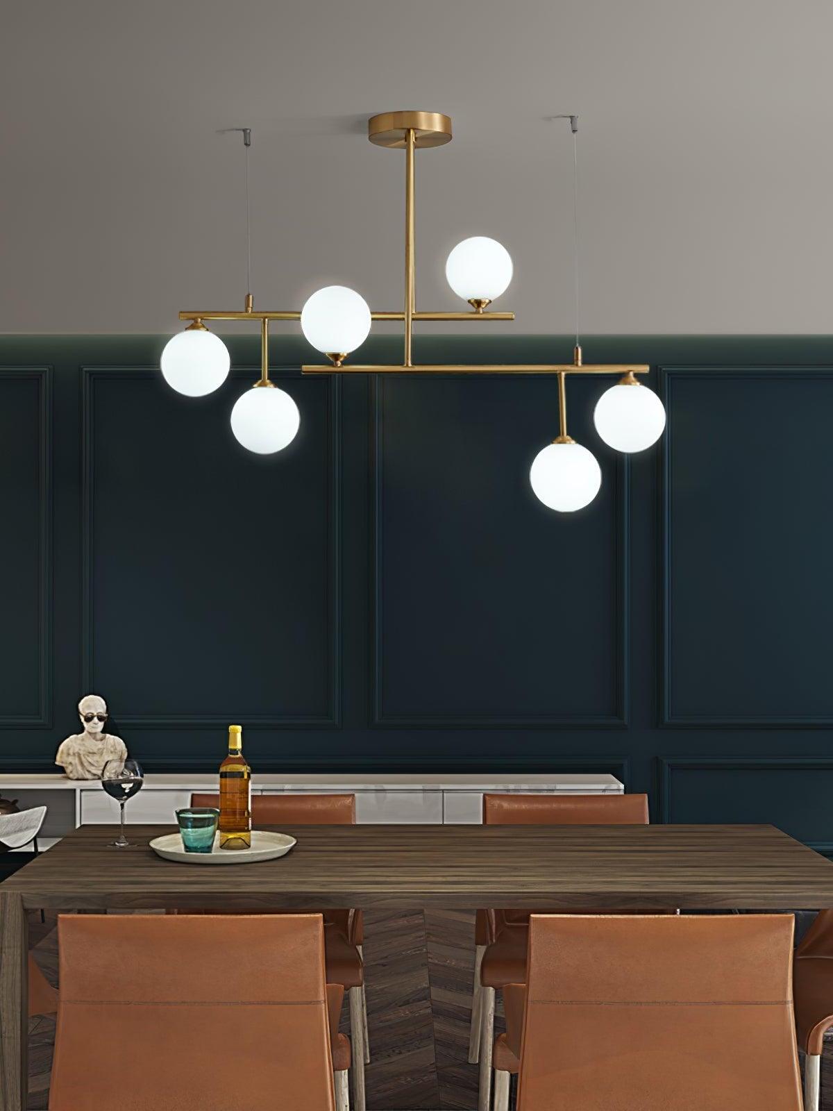 Six white globes on the Arteriors brass-tone frame above a wooden dining table against a dark green panelled wall