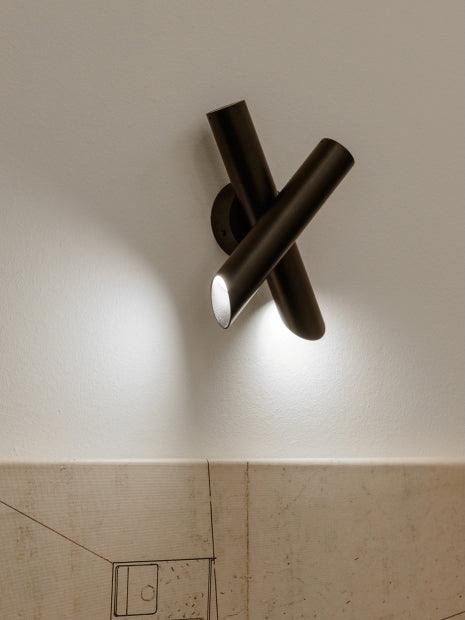 Black crossed-tube lamp above pale tiled wall