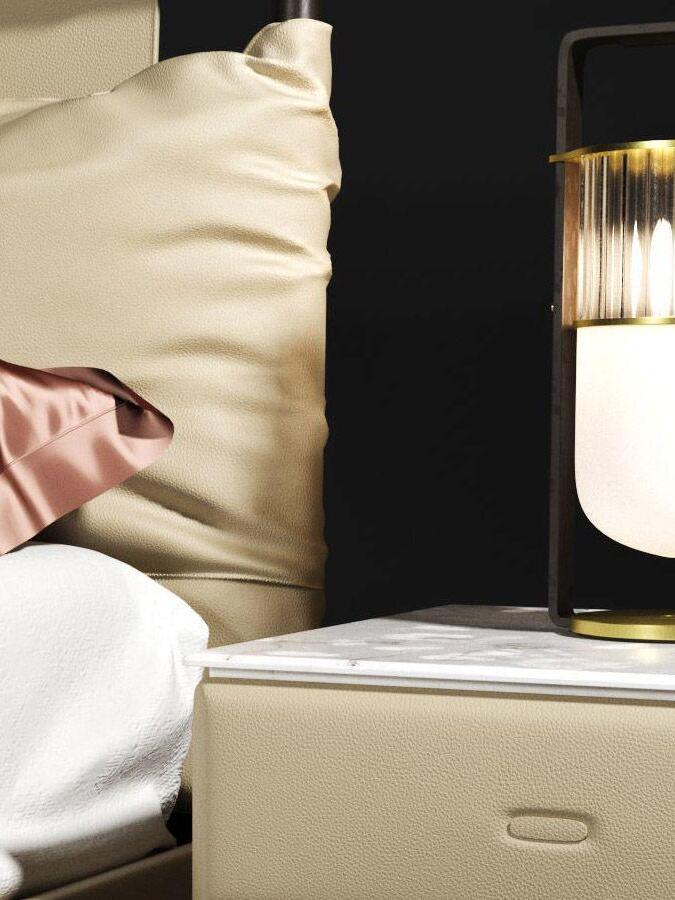 Close cropped Xi lamp on a bedside cabinet next to layered pillows and bedding