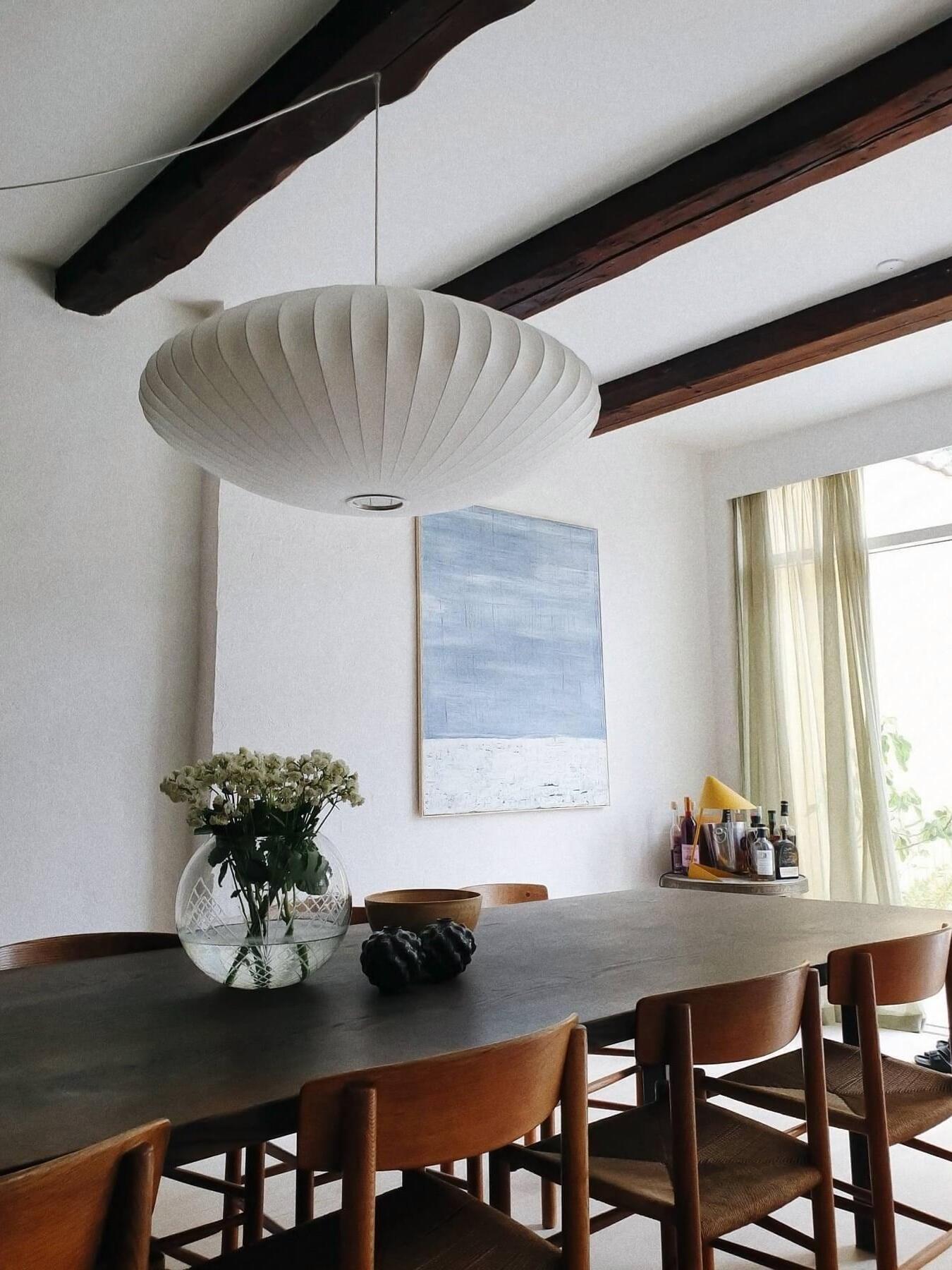 White ribbed bowl-shaped pendant viewed from below above a dining table under dark ceiling beams
