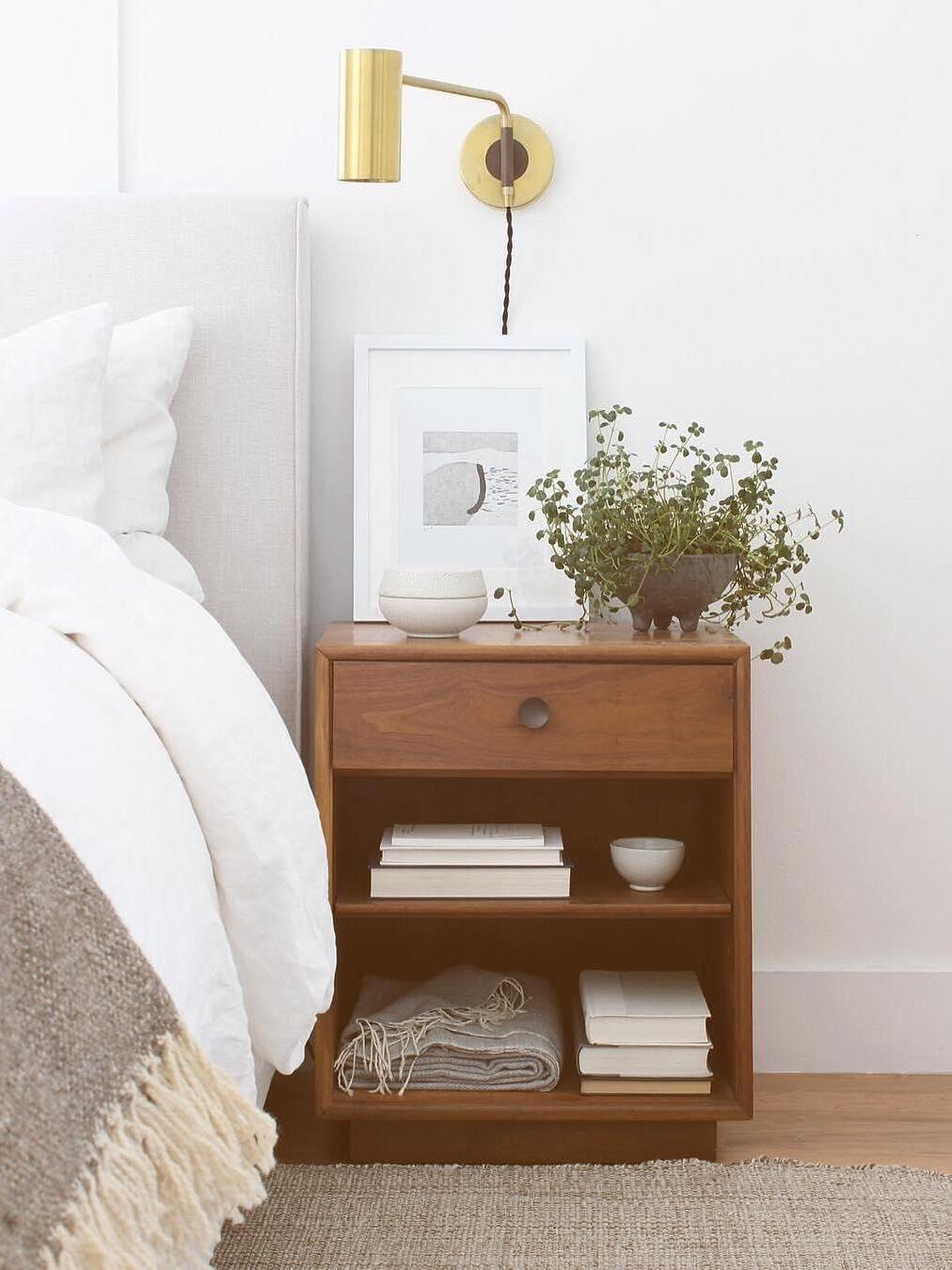 Brass-tone light above wooden nightstand with flowers and picture