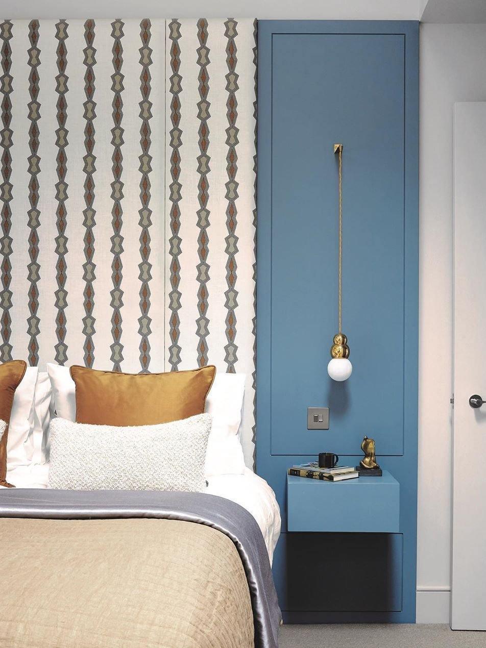 Gold hanging wall light on blue panelling beside a bed