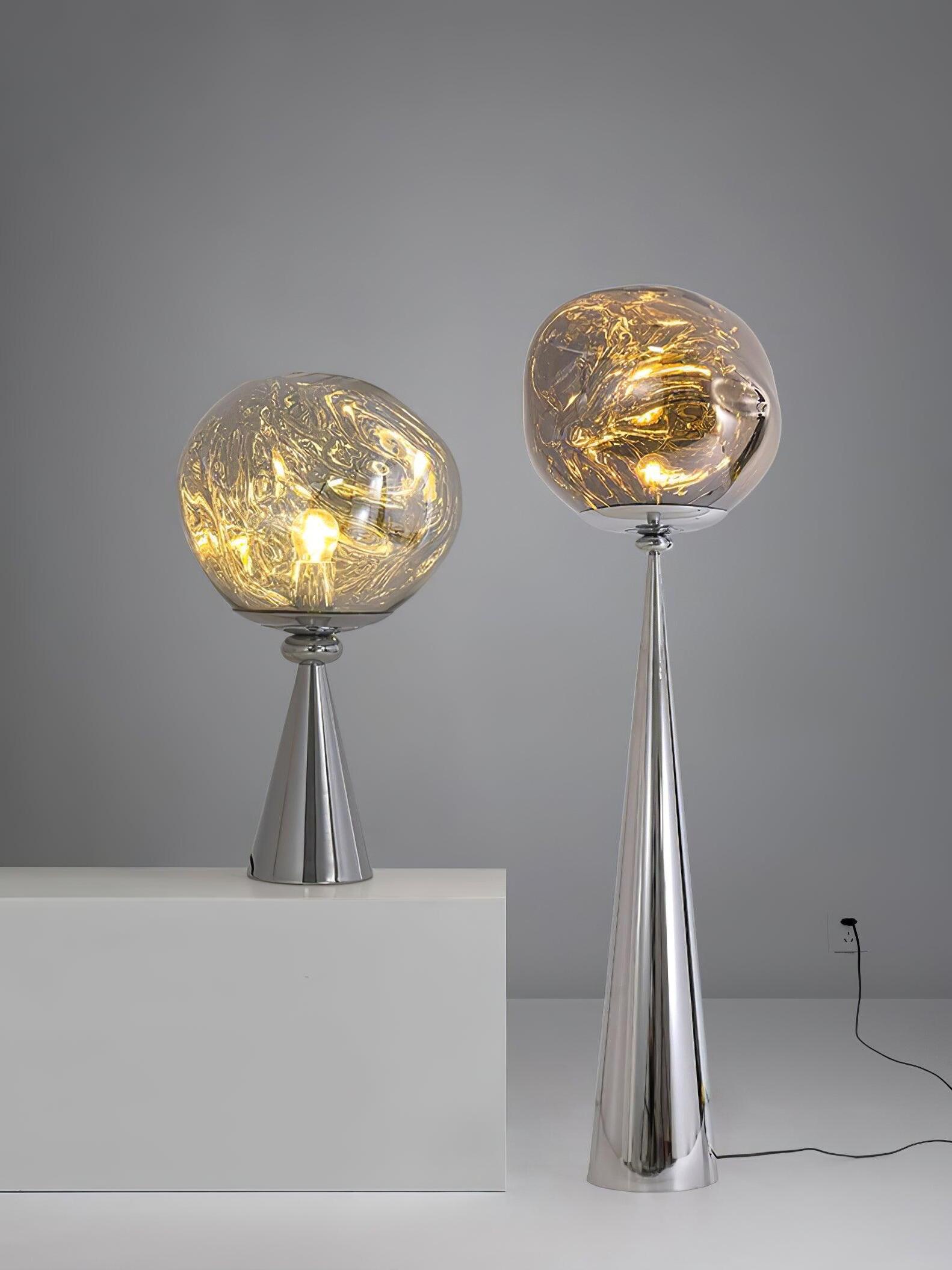 Chrome globe table lamp on a white block beside a taller floor lamp and a visible power cord