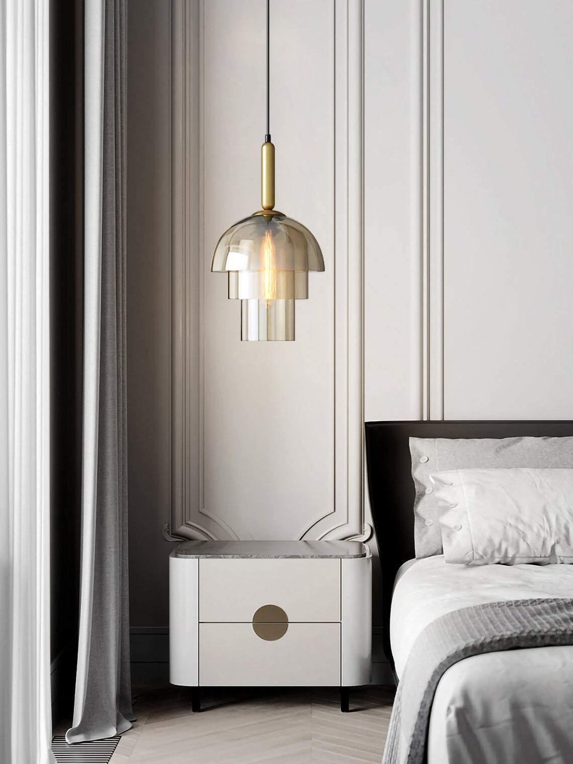 Three-tier glass pendant beside a bed above a white cabinet with gold round handle, grey curtain and panelled wall