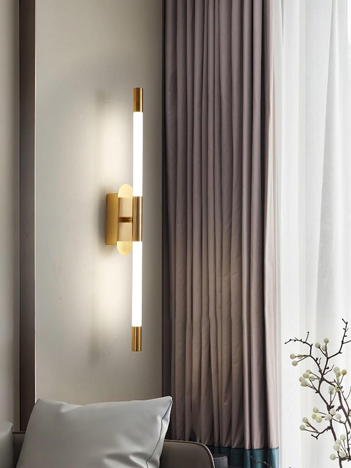 Vertical gold Agnes wall light beside a cushion, tall curtains and a bright window