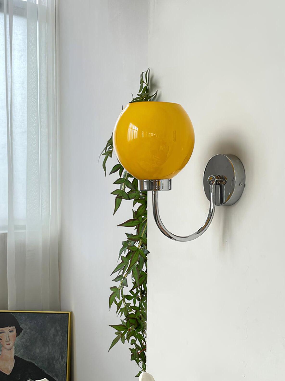 Orange globe above curved wall arm near plant and framed artwork