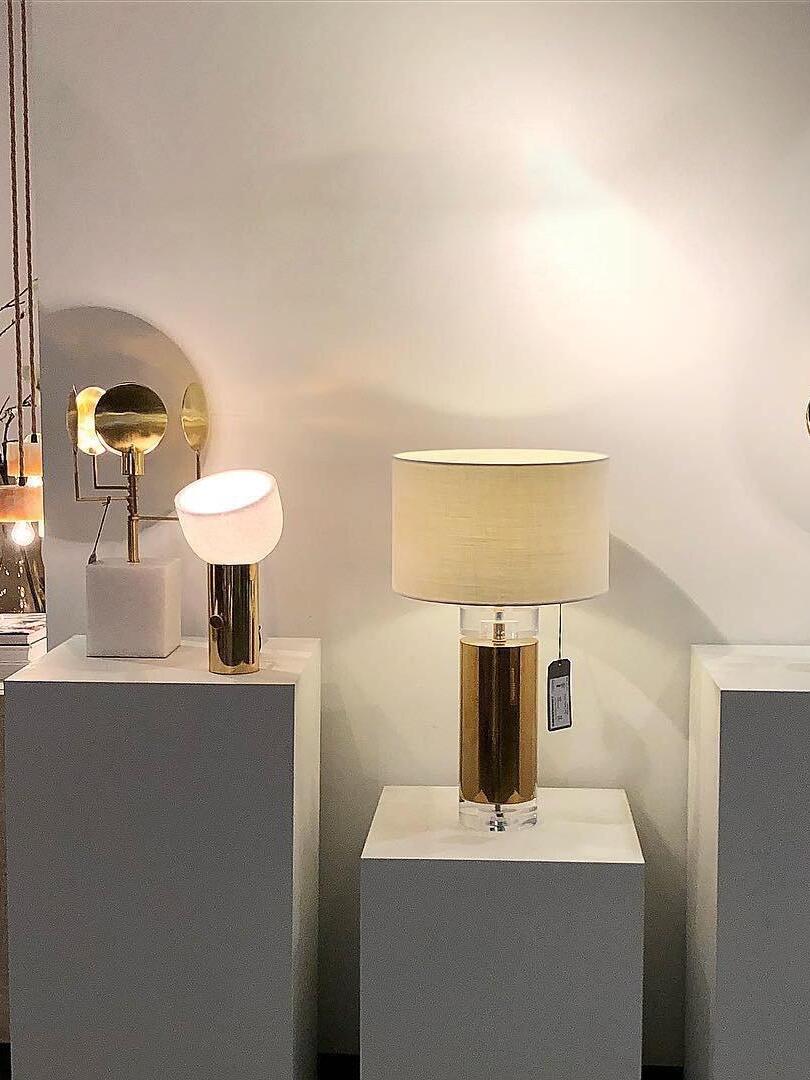 White-shade cylindrical lamp on white display plinth with other lamps behind