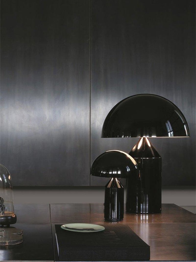 Two glossy black mushroom lamps of different apparent sizes on a wooden cabinet before dark panels