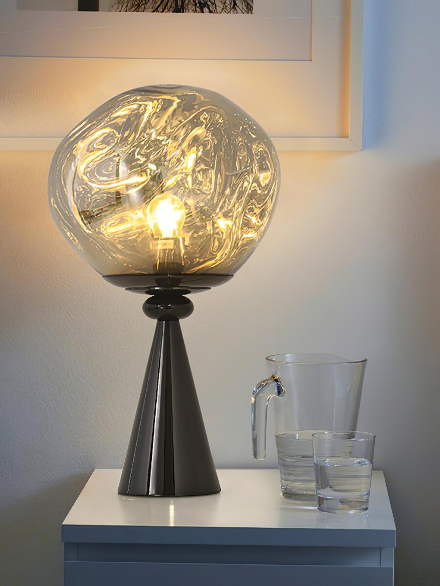 Glowing smoky globe table lamp with a black cone base beside a water jug and tumbler