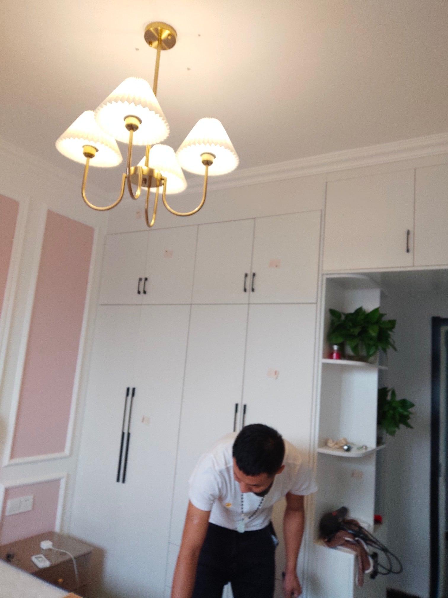 Illuminated chandelier in a pink room with white wardrobes and a person working below