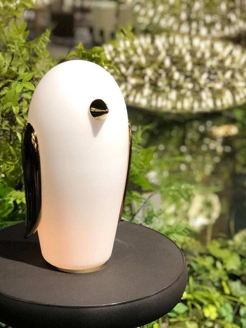 Tall penguin with gold-tone wings on black round table before foliage