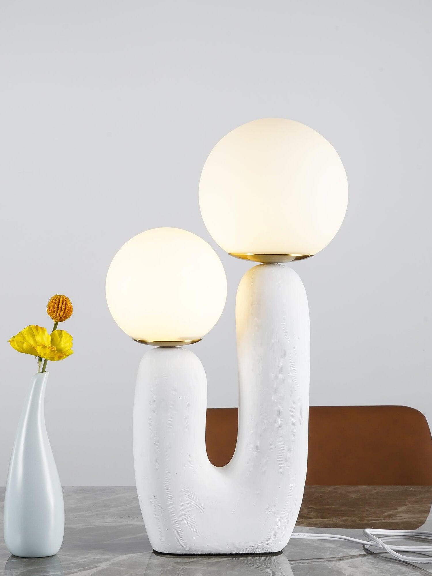 White Oo Rough lamp with glowing opal globes on marble beside pale blue vase and yellow flowers