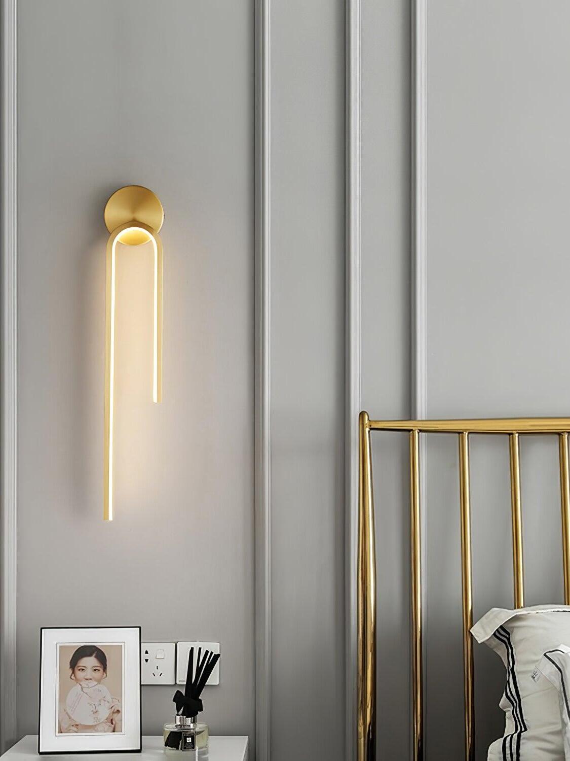 Glowing gold-tone arch with a long left arm beside a gold bed frame and gray paneled wall