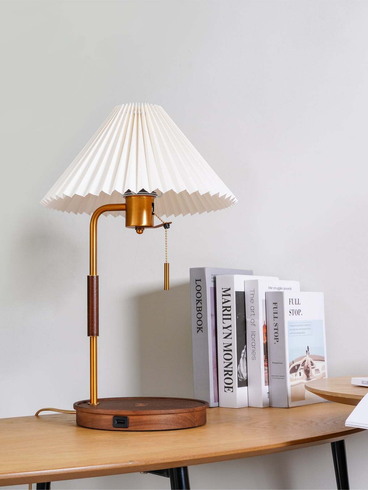 Side view of the white pleated shade, curved upper stem and dark round base on a wooden desk