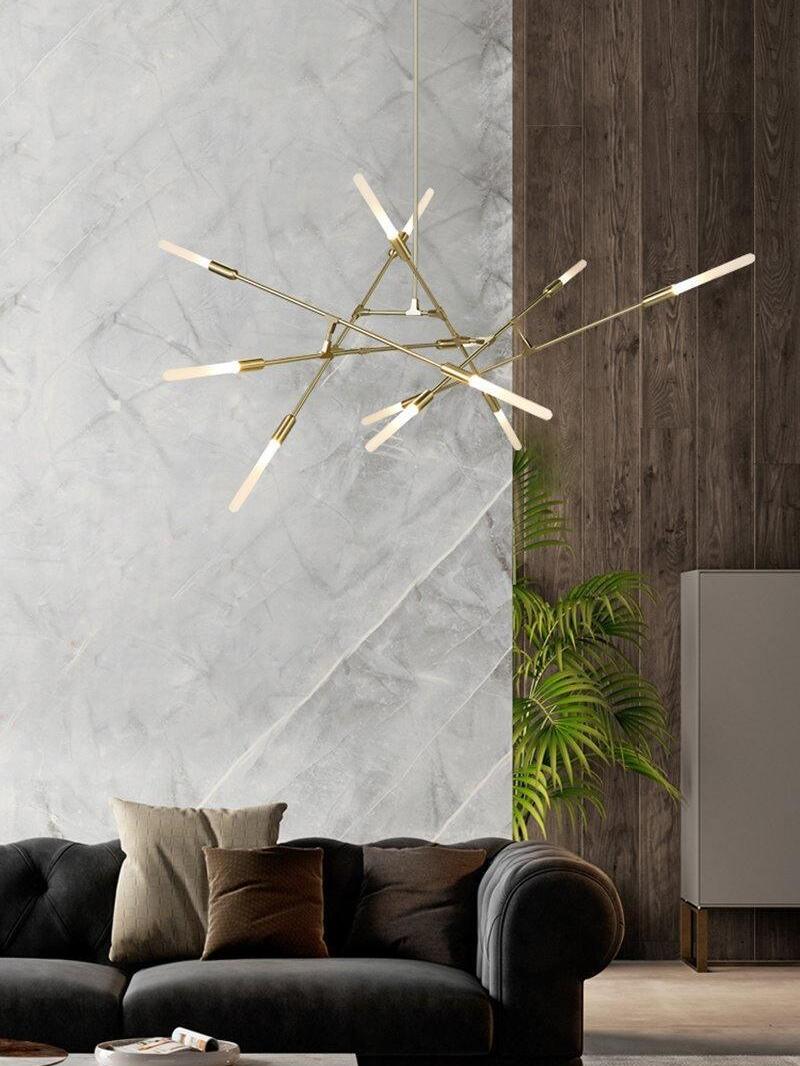 Gold-coloured branching chandelier above a black sofa beside a tall wall