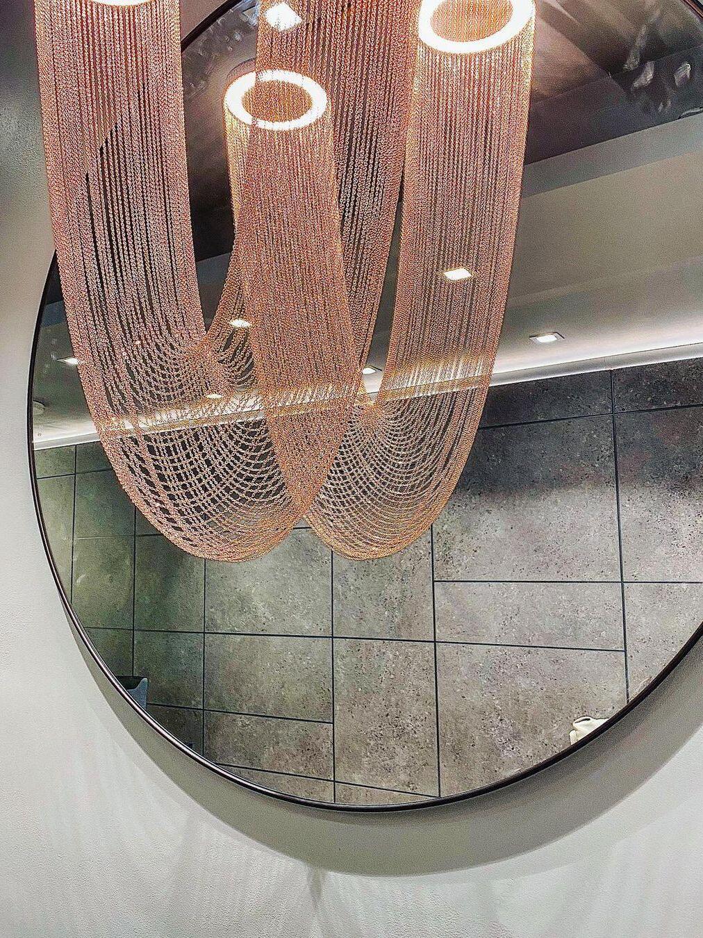 Rose-gold chain loops reflected in a round mirror