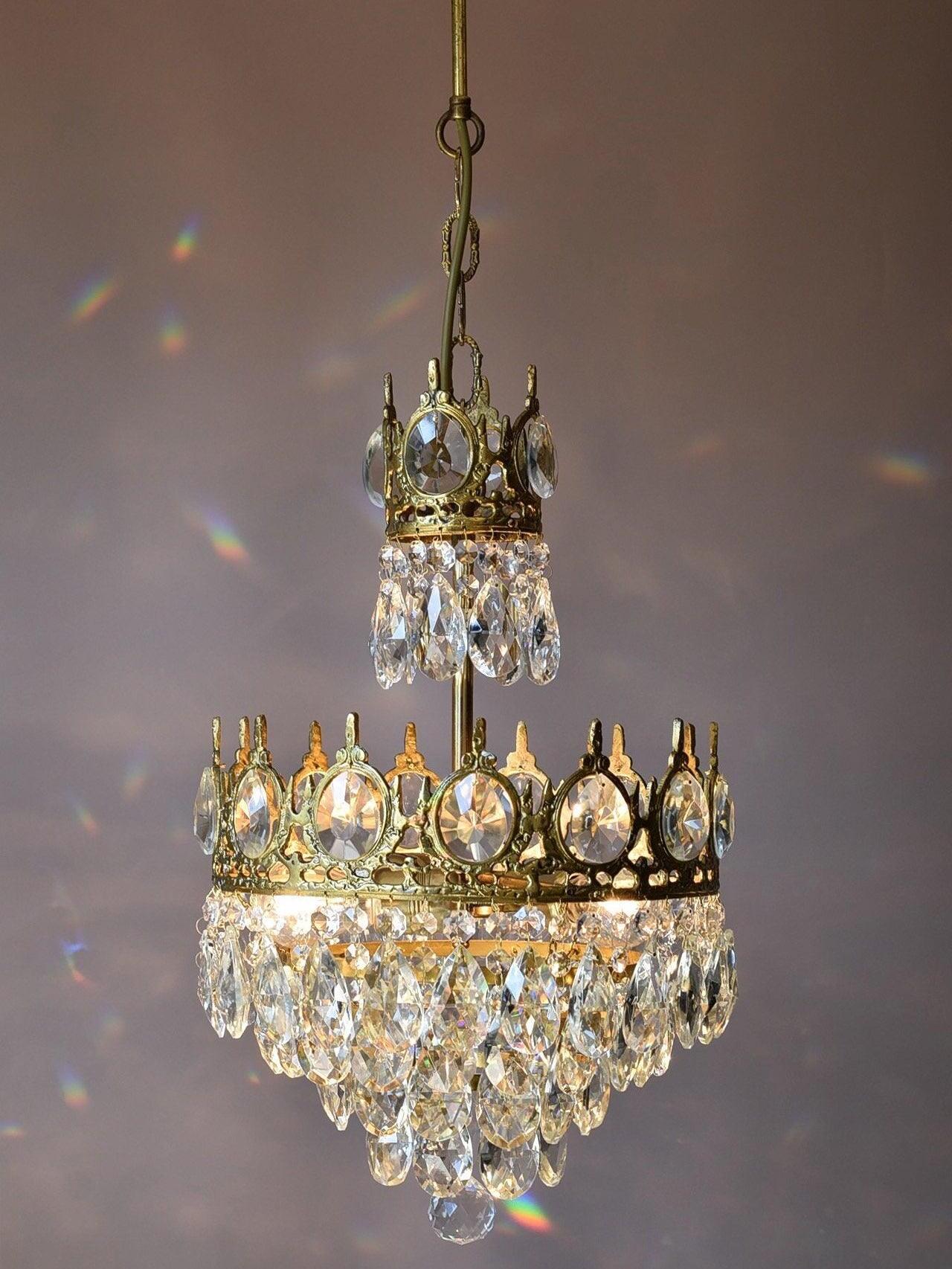 Illuminated crystal chandelier on a visible chain with coloured reflections around its two crown sections